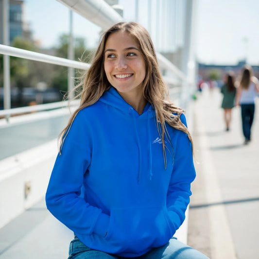 Smiling woman in blue mountain graphic hoodie on a city bridge, streetwear fashion