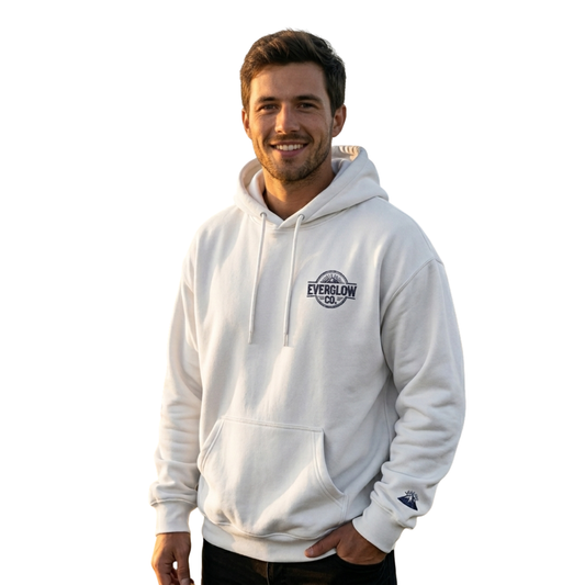 A man with short brown hair and a beard is smiling against a white background, wearing a white Nightfall Summit – Embroidered unisex relaxed fit hoodie and dark pants.