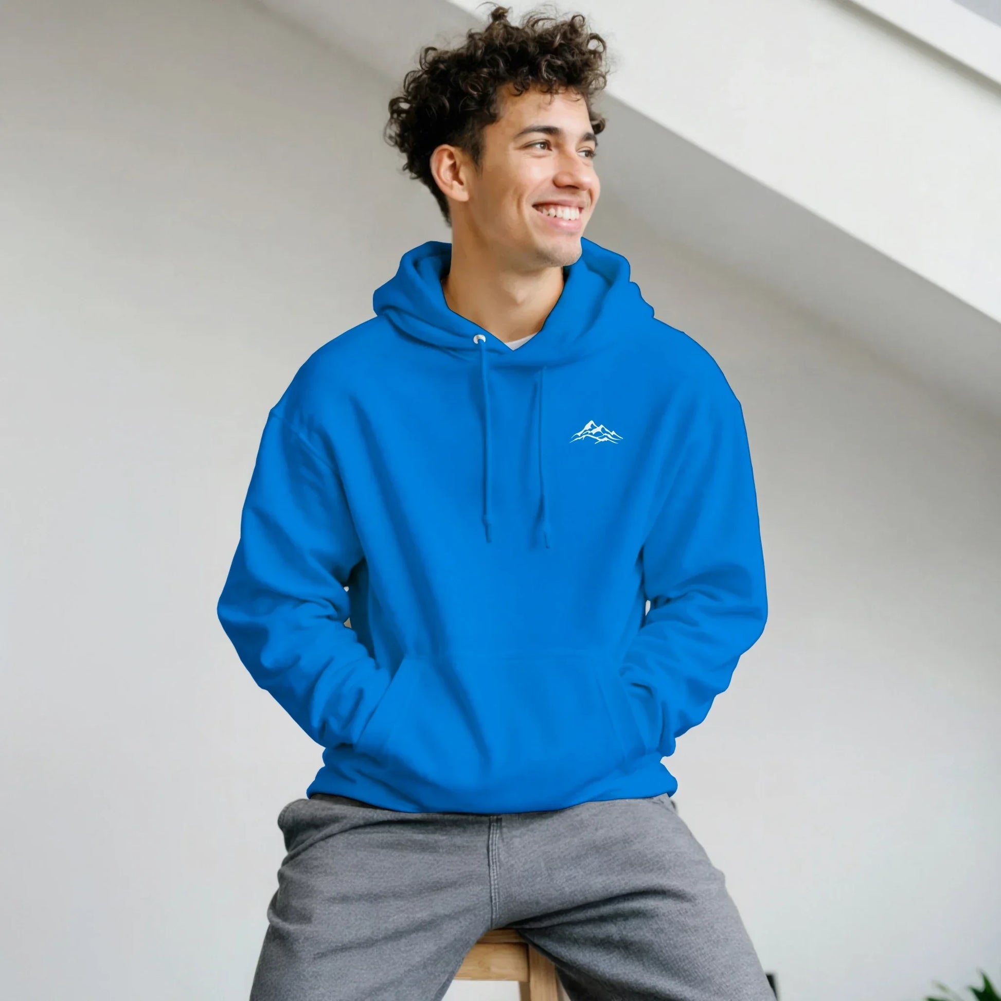 Smiling man wearing blue mountain graphic hoodie and gray sweatpants indoors