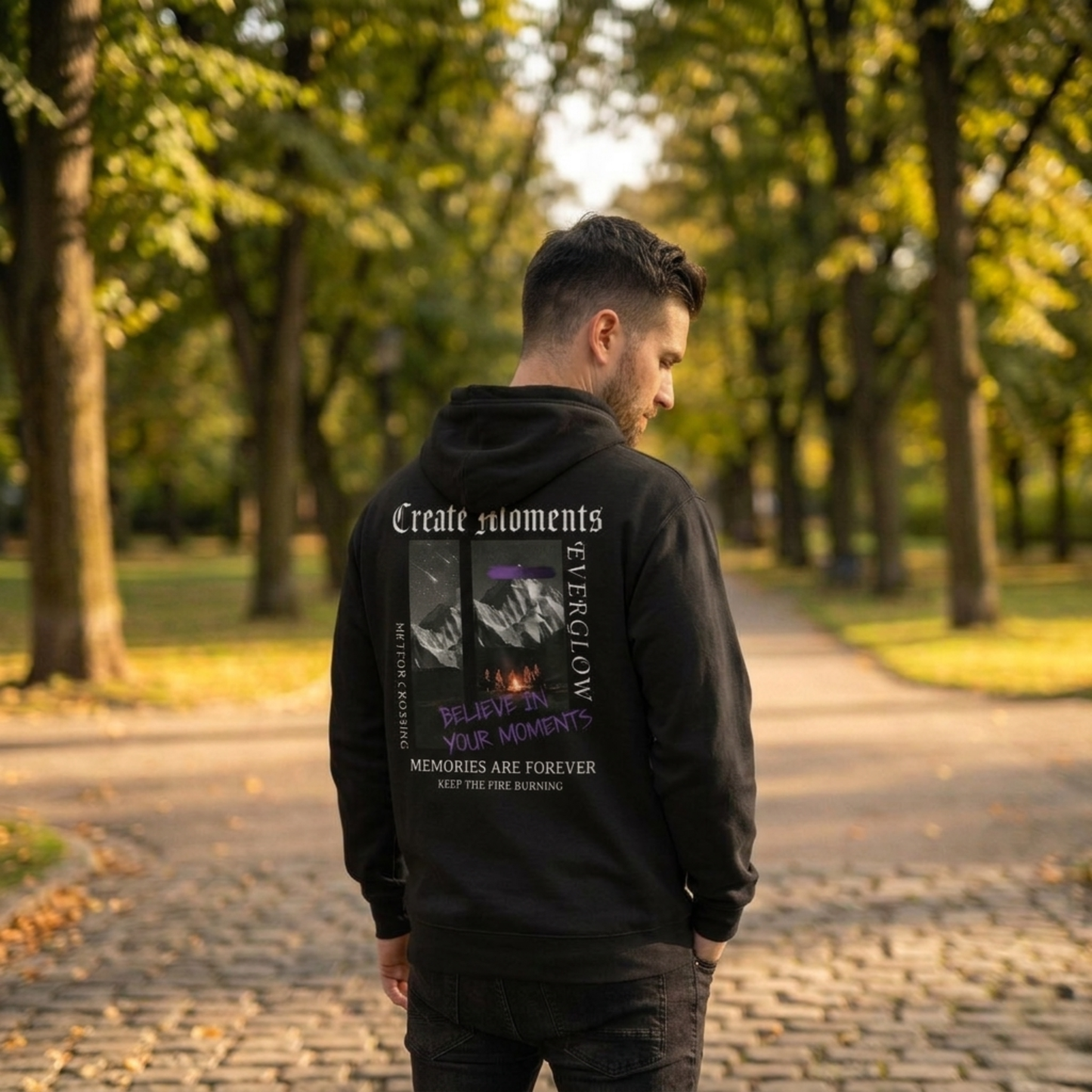A man stands on a tree-lined park path wearing the Create Memories Hoodie, featuring cozy fleece fabric and graphic text on the back, including phrases like "Create moments," "Believe in your moments," and "Memories are forever.