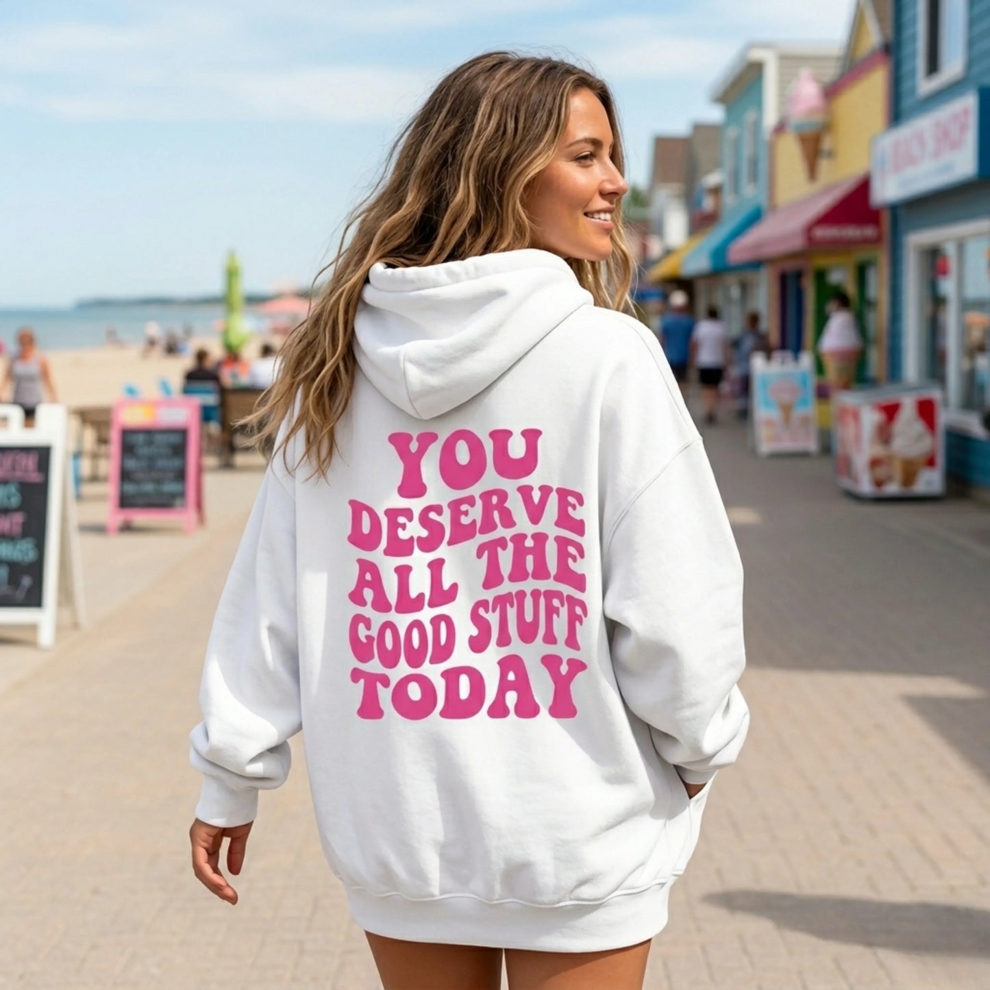Woman wearing white hoodie with pink motivational quote on boardwalk by the beach