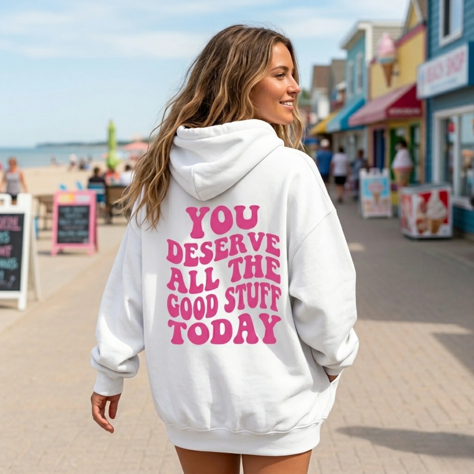 Woman wearing white hoodie with pink motivational quote on boardwalk by the beach