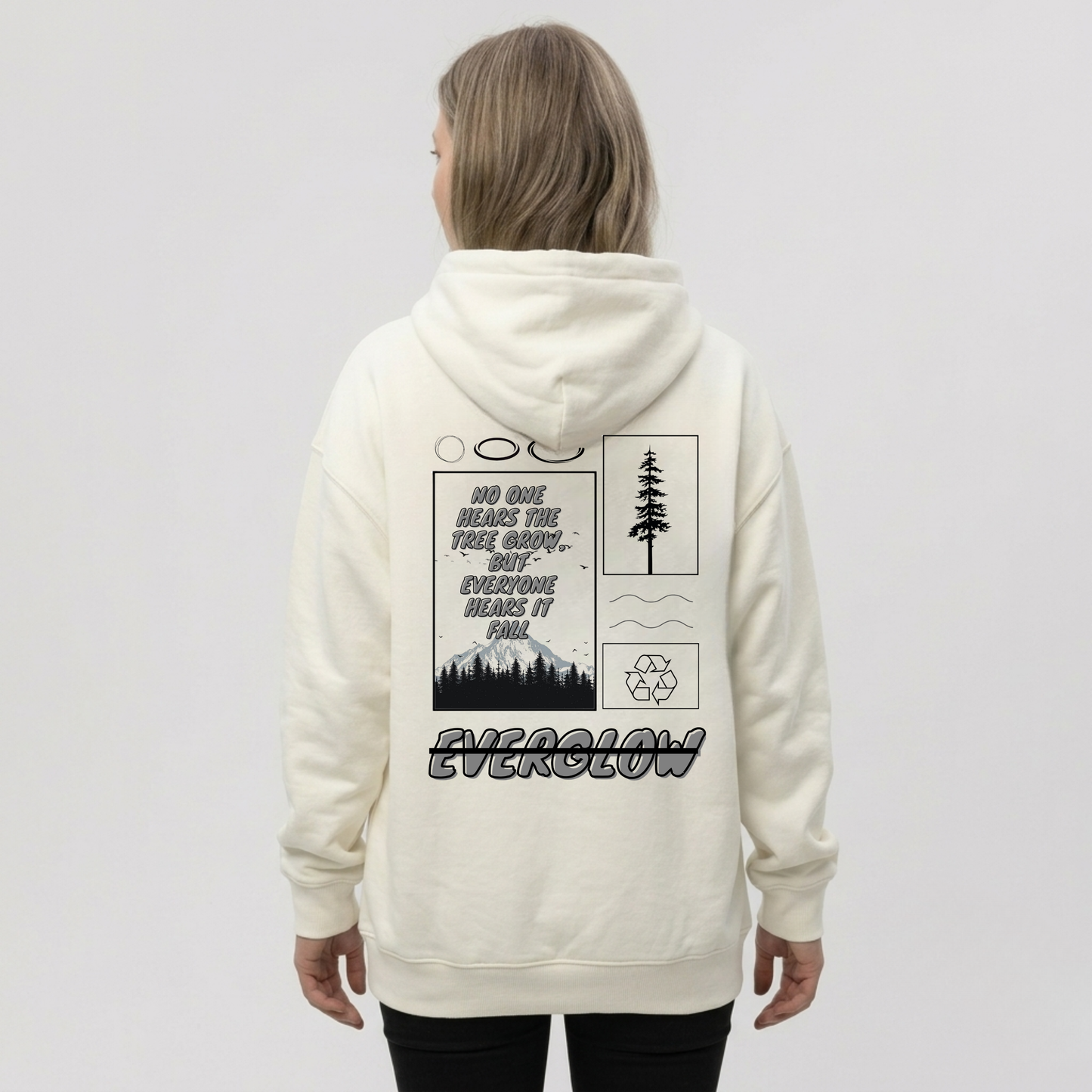 A person wears the Everglow: Silent Growth cozy fleece hoodie with graphic designs of trees, mountains, a recycling symbol, and the words "No one hears the tree grow…but everyone hears it fall" and "EVERGLOW" on the back.