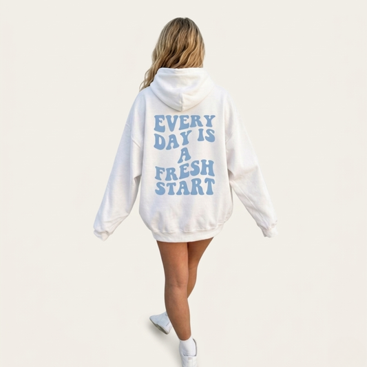 A person with long blonde hair wears the Fresh Start Hoodie with blue "EVERY DAY IS A FRESH START" text, standing against a plain light background.