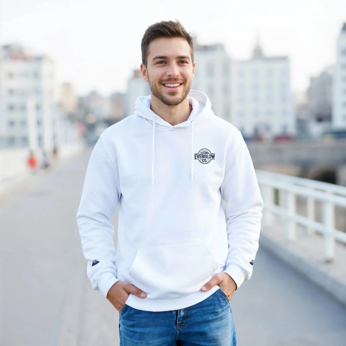 Man in white mountain-themed graphic hoodie and jeans outdoors, casual streetwear style