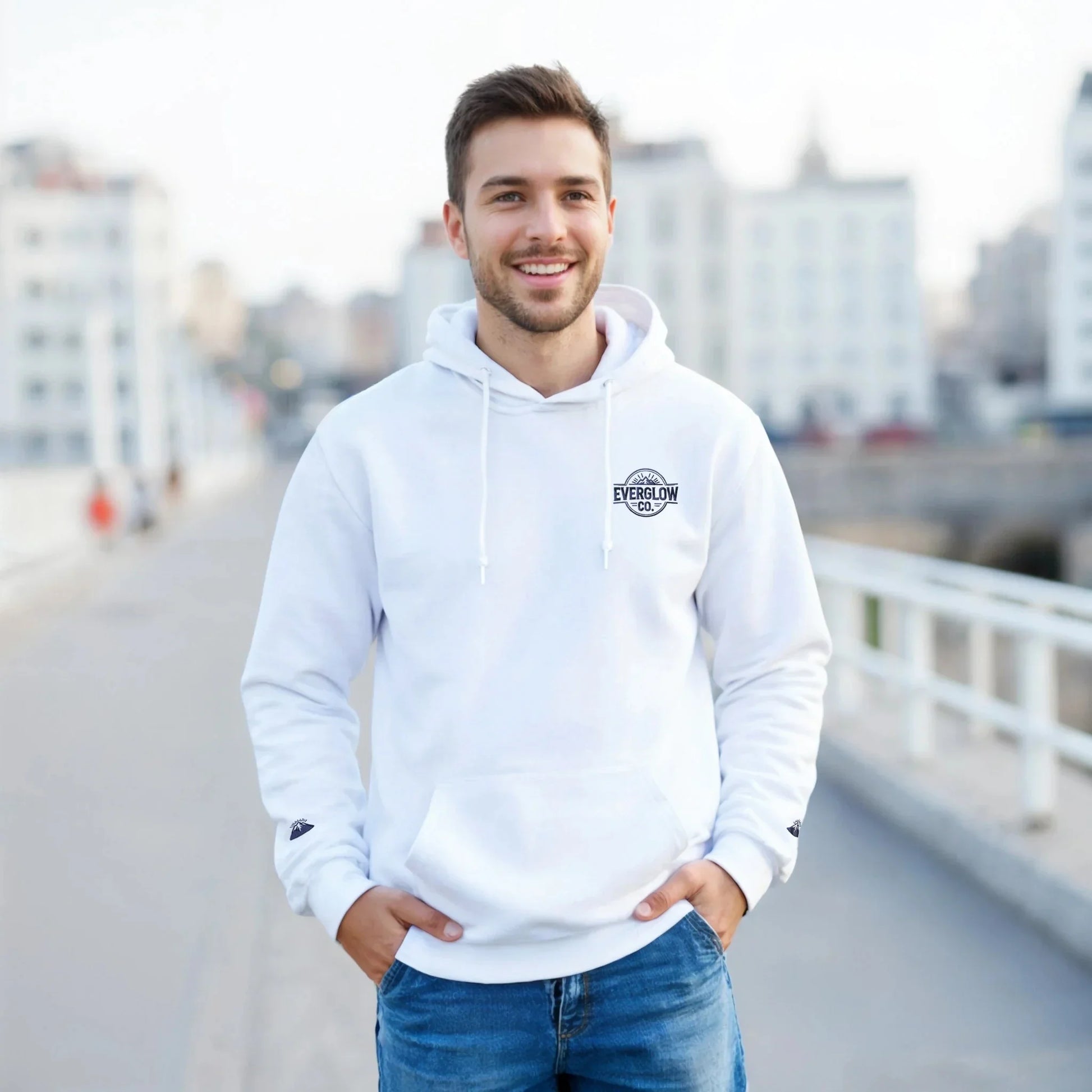 Man in white mountain-themed graphic hoodie and jeans outdoors, casual streetwear style