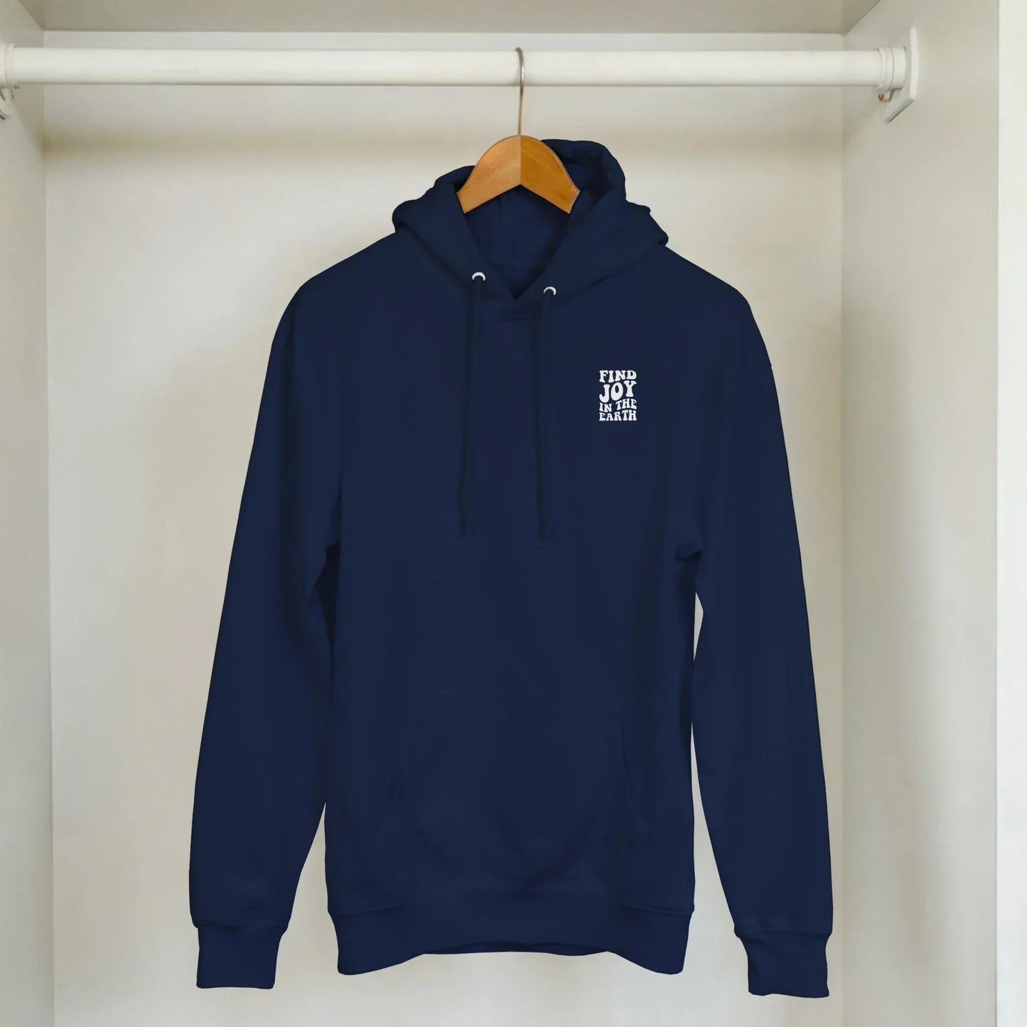 Navy blue unisex hoodie with 'Find Joy In The Earth' nature graphic, hanging in closet