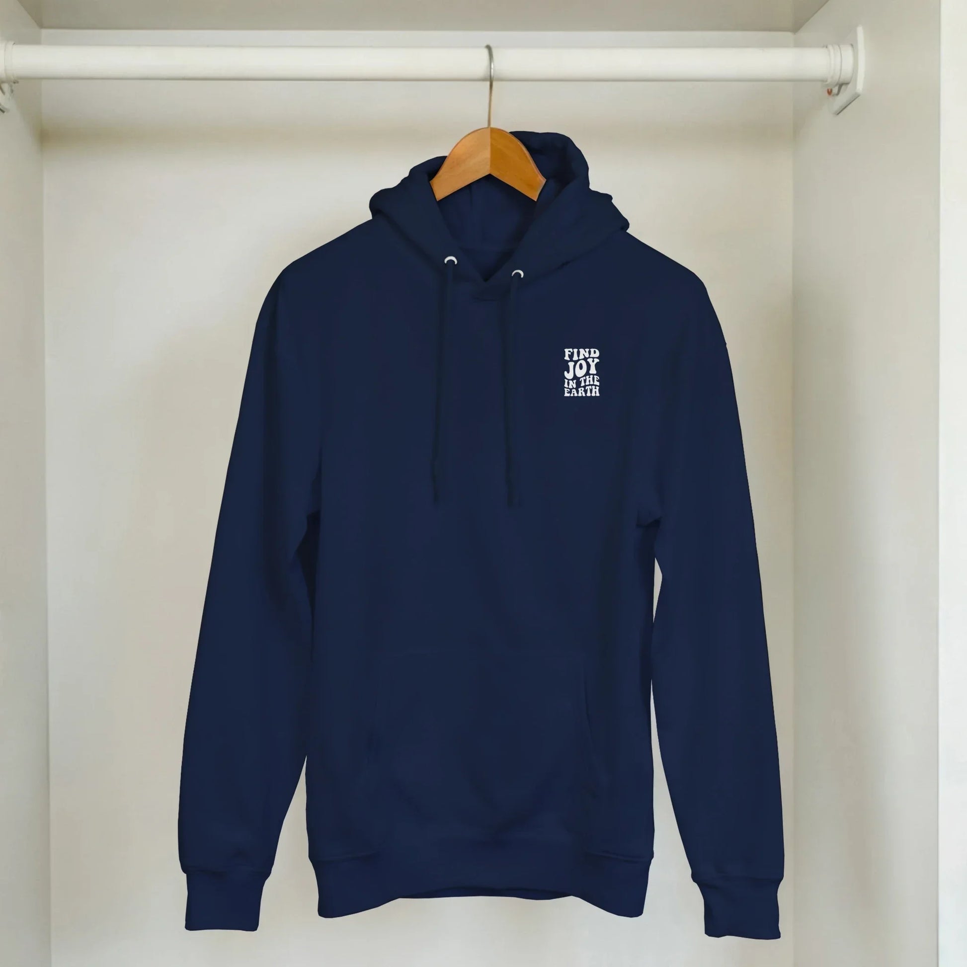 Navy blue unisex hoodie with 'Find Joy In The Earth' nature graphic, hanging in closet